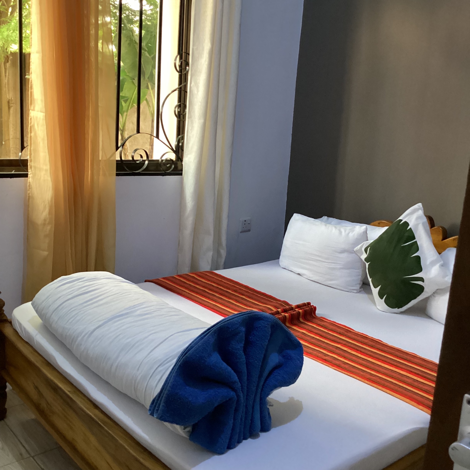 A guest room at AIM Lodge in Arusha with a wooden bed and sunlit curtains